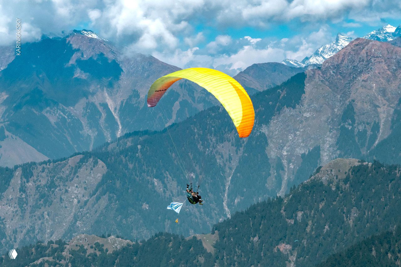 Жёлто-оранжевый параплан вблизи на фоне высоких гор и облаков — широкий план с подчёркнутой перспективой и рельефом Гималаев.