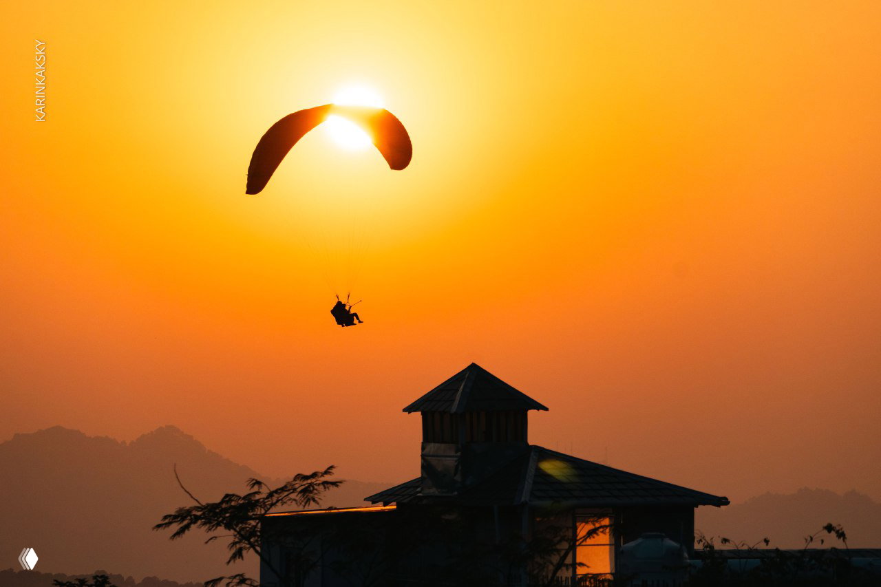 Парапланерист на закате, силуэт на фоне яркого солнца и оранжевого неба создаёт драматичную композицию и тёплое настроение.