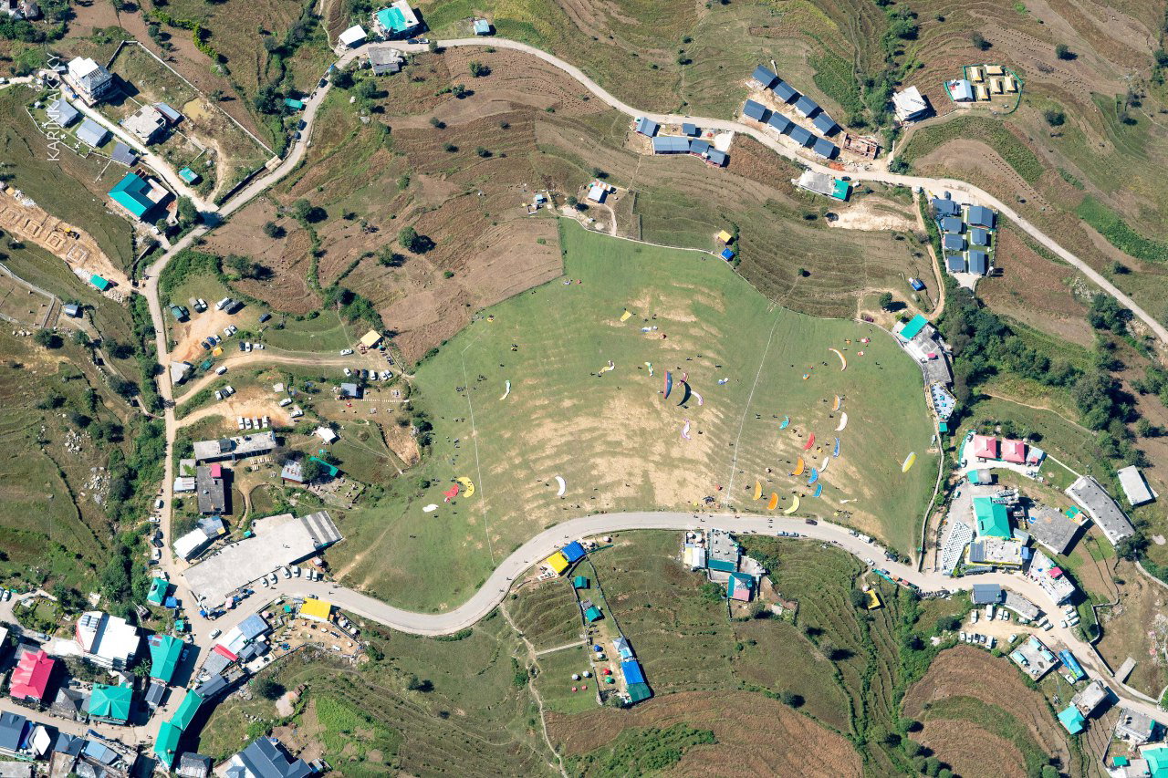 Аэровид сверху: поляна старта и множество парапланов на земле, участники фестиваля и логистика внизу.