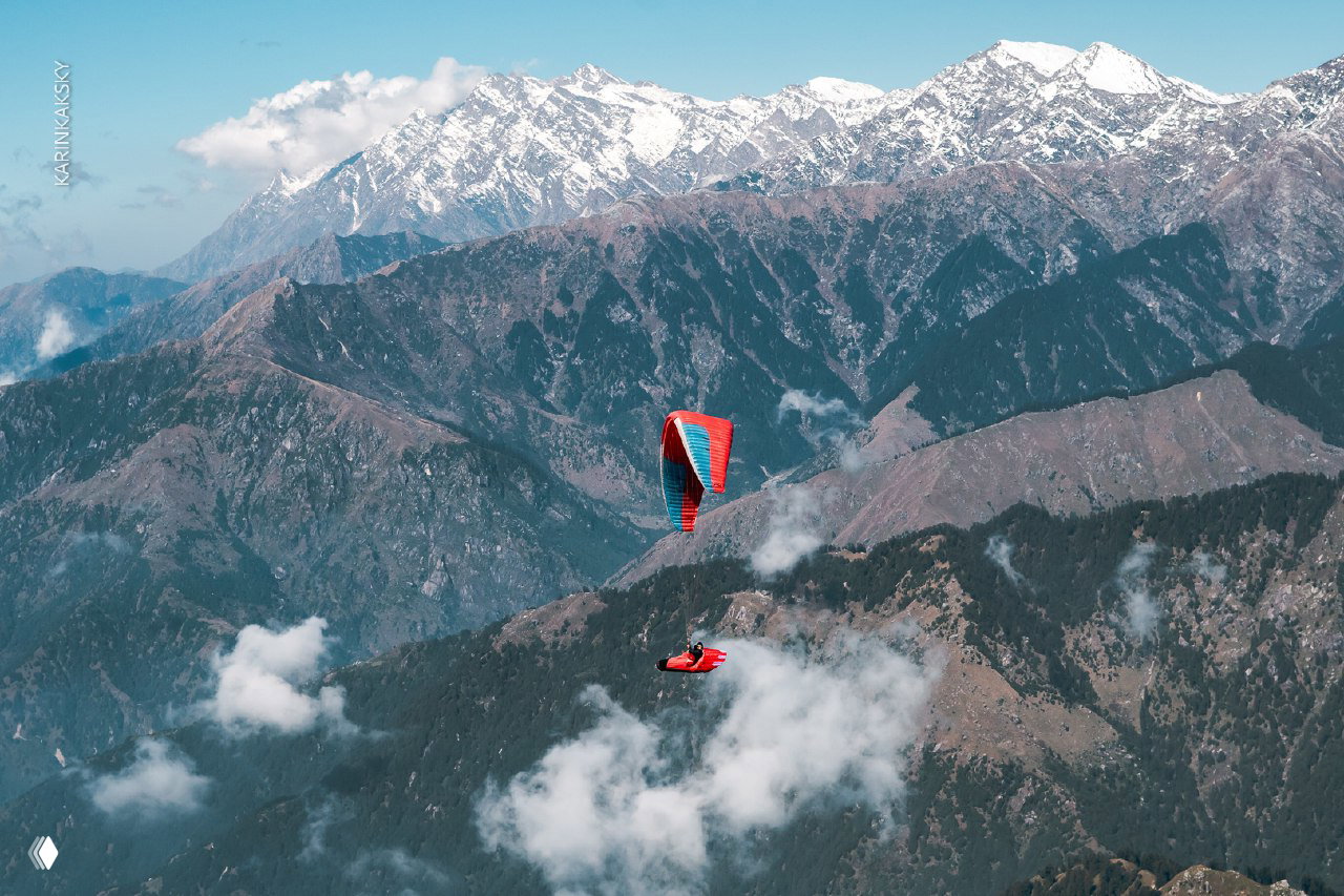 Параплан в полёте над глубокими долинами и горными хребтами, красное крыло на фоне величественных гималайских вершин.