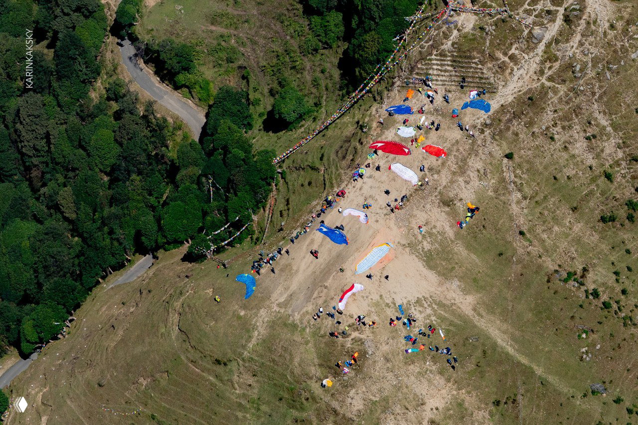 Вид сверху на стартовую площадку: расстиленные купола, экипаж и подготовка к полётам — цветные крыла на земляной площадке у обрыва.