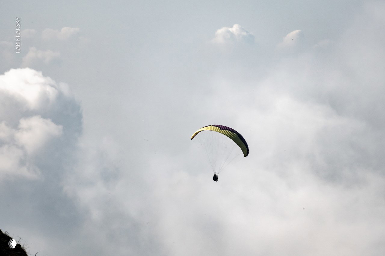 Параплан в полёте на фоне плотного слоя облаков; силуэт пилота крупным планом и рассеянный свет сквозь облачную массу.