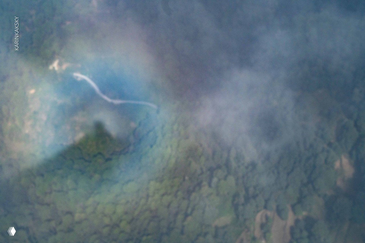 Крупный план природной глории над зелёным лесом: радужное кольцо вокруг тёмной тени человека на облаке и извилистая тропа внизу.