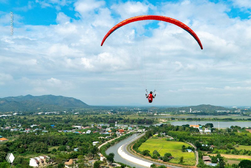 Параплан в полёте над дорогой, холмами и озёрами; панорамный вид сельского ландшафта Таиланда с подвесной системой пилота.