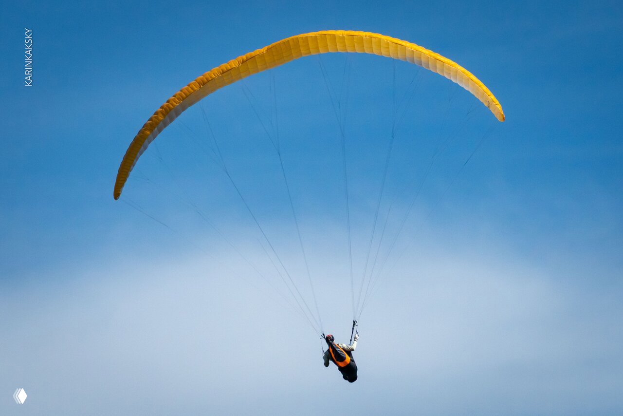 Жёлтое крыло параплана красиво раскрыто на фоне чистого неба и лёгкой облачности; пилот висит в подвесе — кадр с групповых полётов в Таиланде.