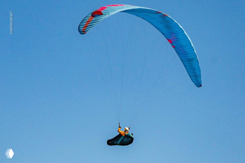 Один парапланист в синих тонах купола парит на чистом небе, кадр подчёркивает силуэт пилота и спокойствие воздушного пространства.