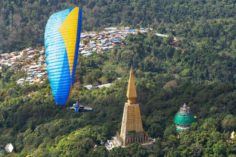 Параплан над зелёным холмом и городской застройкой внизу; вид с высоты показывает сочетание природы и населённого пункта у маршрута.