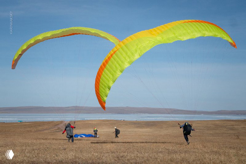 Несколько парапланов на старте и люди на земле готовят крылья: наземная работа с парапланом в практическом упражнении.