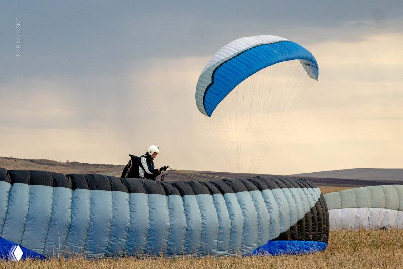 Пилот сидит в подвесной системе у надувного параплана на земле: тренировка контроля купола и подготовка к запуску.