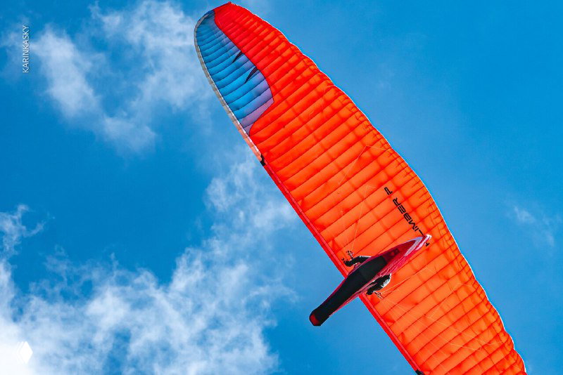Яркое красно‑синее крыло параплана в полёте над чистым небом в Таиланде; вид снизу на профиль пилота и контраст голубого фона.