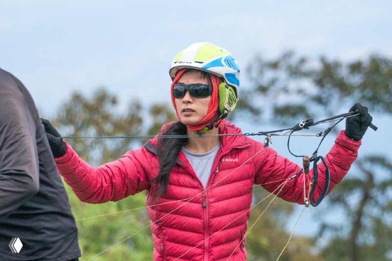 Инструктор или участник в шлеме готовит стропы параплана перед запуском; фокус на руках, экипировке и подготовке на старте в Таиланде.