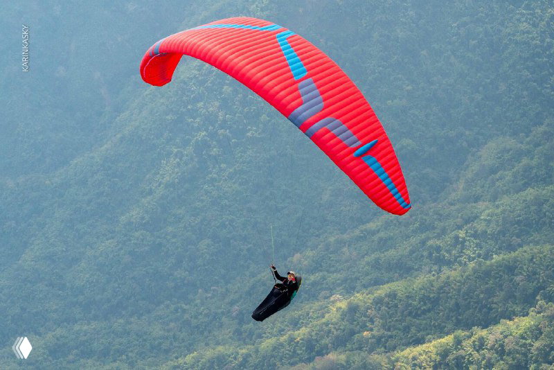 Красное крыло парящего пилота на фоне холмистой горной местности и туманных склонов; панорама джунглей и рельефа вокруг в Таиланде.