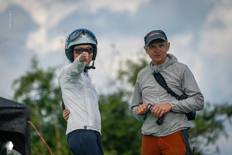Два пилота в шлемах и ветровках обсуждают маршрут и погодные условия перед вылетом — кадр с тренировочного выезда по параплану в Таиланде.