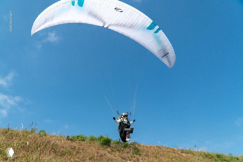 Парапланист на травянистом склоне с раскрытым крылом в момент старта — взлёт с холма во время тренировочного налёта в Таиланде.