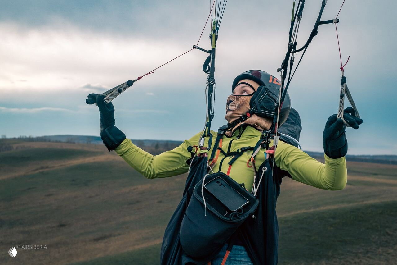 Тандемный полёт на параплане над бескрайними полями: пассажир в амуниции смотрит в небо, мягкая сибирская степь внизу.