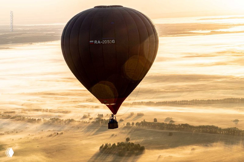 Крупный план тёмного воздушного шара с видимыми регистрационными символами на фоне мягкого солнечного света и рассеивающейся росы.