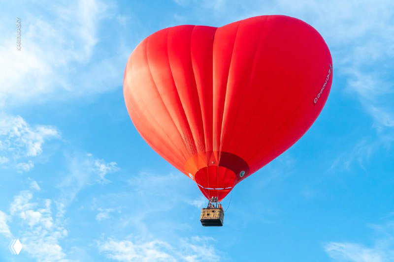 Яркий красный воздушный шар в форме сердца на фоне чистого голубого неба, эффектная композиция для фотосессии в воздухе.