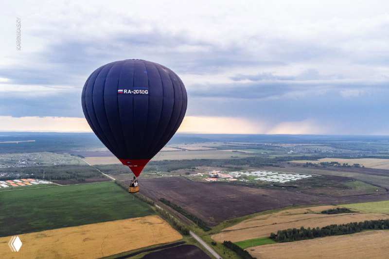 Воздушный шар над разноцветными полями и дорогой, панорамный аэрофотоснимок с высоты показывает череду сельскохозяйственных участков.