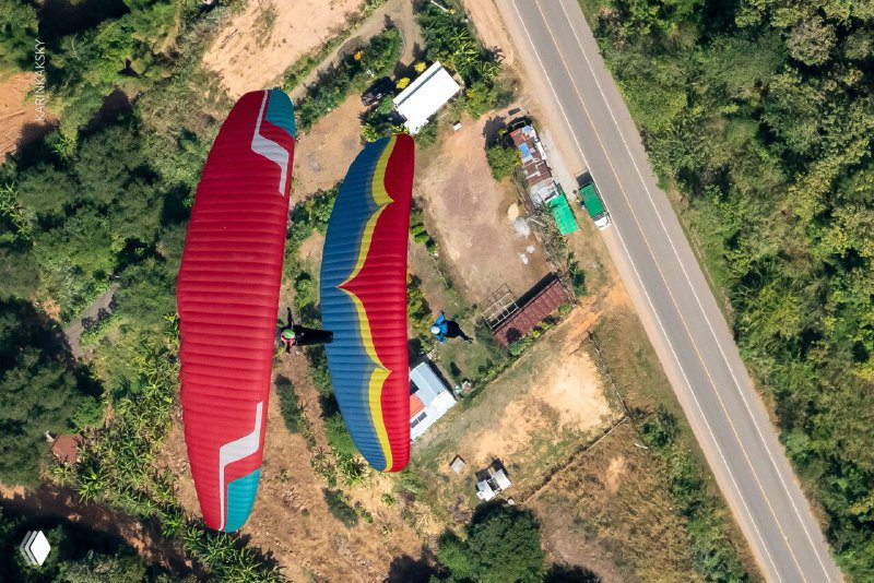 Два красно-голубых параплана парят над обочиной дороги и участками земли в Таиланде: аэросъёмка с видом вниз на пейзаж.