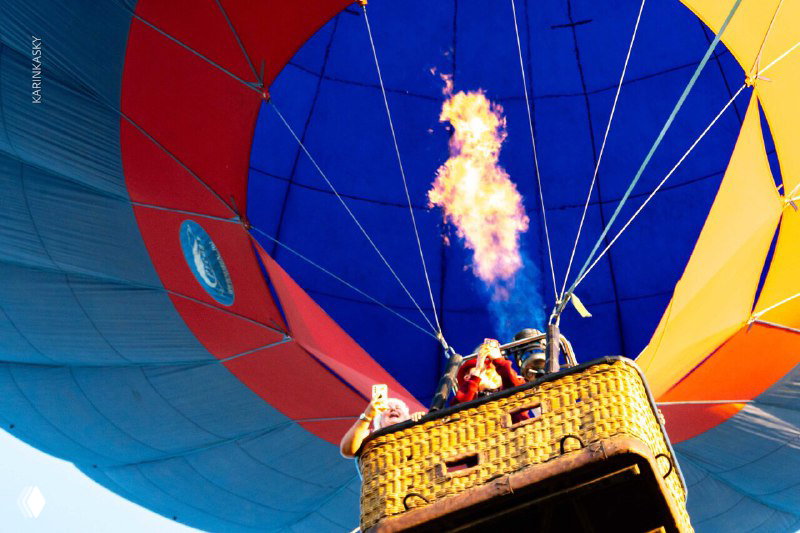 Вид снизу на раскрытую разноцветную оболочку воздушного шара и горелку с пламенем: контраст ярких сегментов ткани и огня.