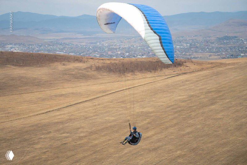 Пилот на параплане летит над холмом с видом на долину и город вдалеке: сочетание ландшафта и техники парения на крыле.