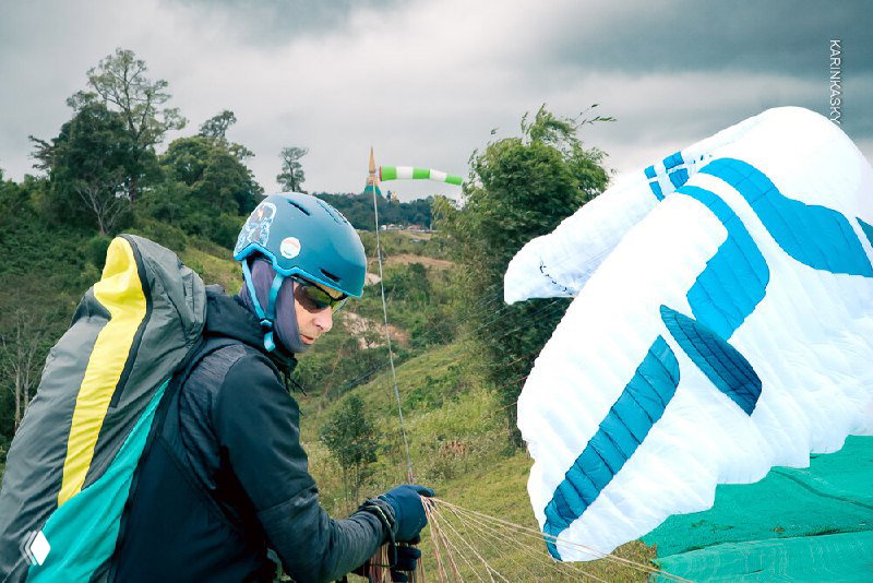 Инструктор готовит снаряжение и параплан к старту на турбазе — вид крупным планом на шлем и купол на земле.