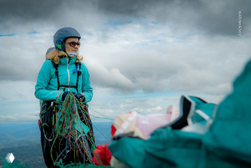 Участник с парапланерным креслом, глядущий вдаль над облаками — кадр, подчёркивающий ожидание и сосредоточенность перед полётом.