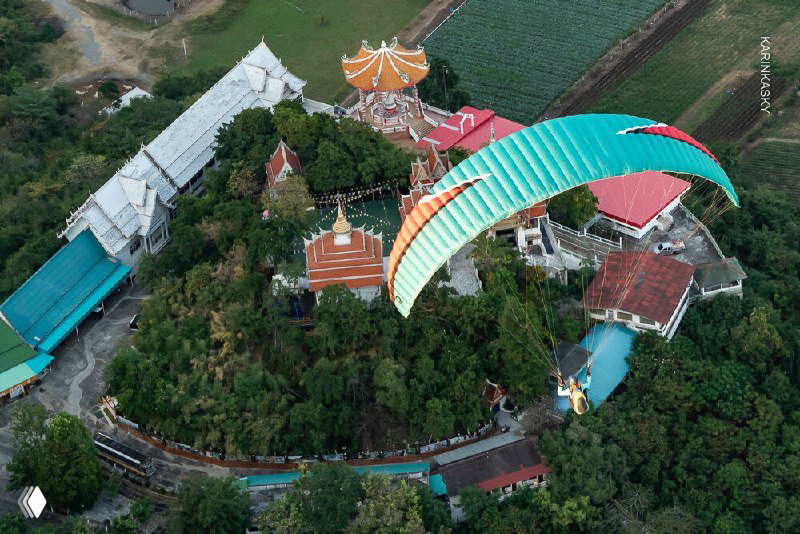 Парапланер совершает пролёт над кроной деревьев и домами на холме — вид сверху на маршрут и местные постройки.