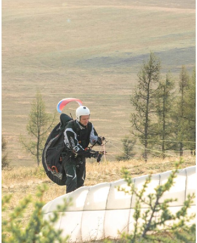 Пилот идёт по склону с куполом позади, контролируя стропы и оборудование перед очередным запуском в условиях полевого тренировочного интенсива.