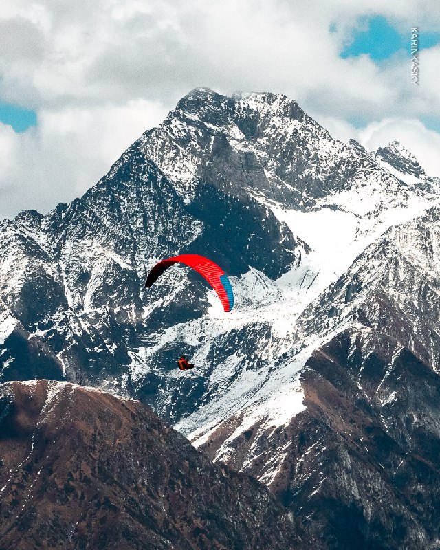 Параплан над заснеженной горной вершиной; красочный купол контрастирует с суровым рельефом и высокогорной атмосферой.