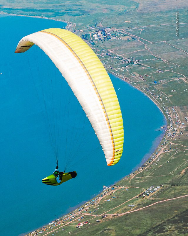 Параплан над береговой линией и бухтой; съёмка сверху демонстрирует крыло, море и прибрежную полосу — хороший маршрут для увеличения налёта.
