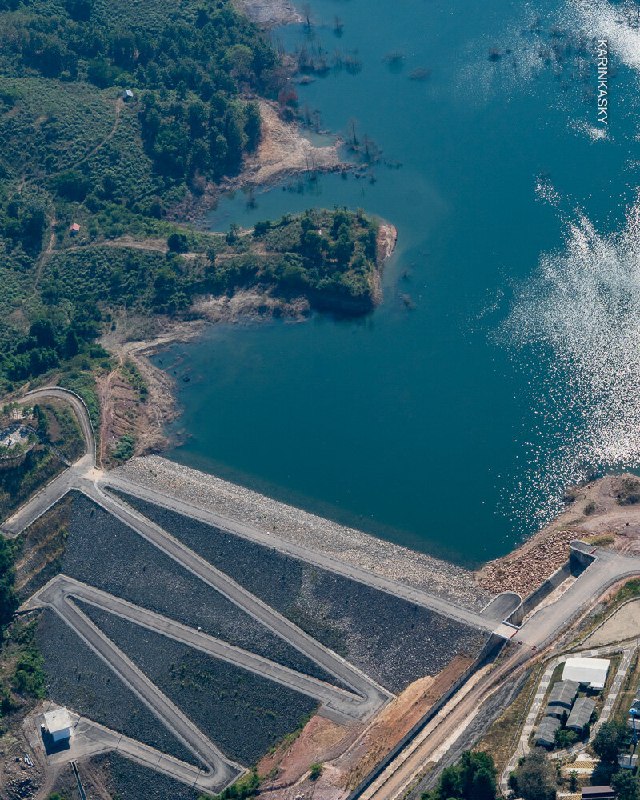 Вид сверху на водохранилище и плотину, рядом — параплан в небе; сочетание воды, инфраструктуры и полёта создаёт интересный ракурс.