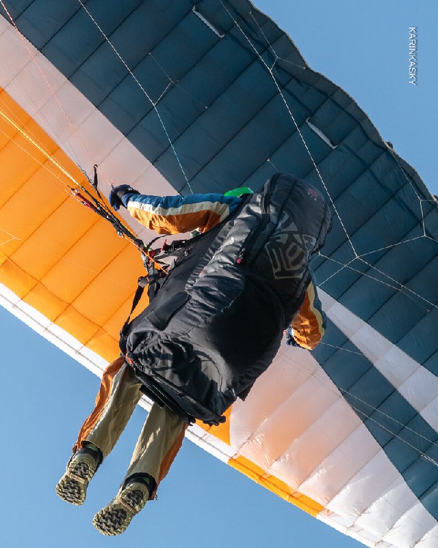 Крупный план подвески и ног пилота под куполом тёплых оттенков; снимок демонстрирует конструкцию подвесной системы и безопасное расположение ног.