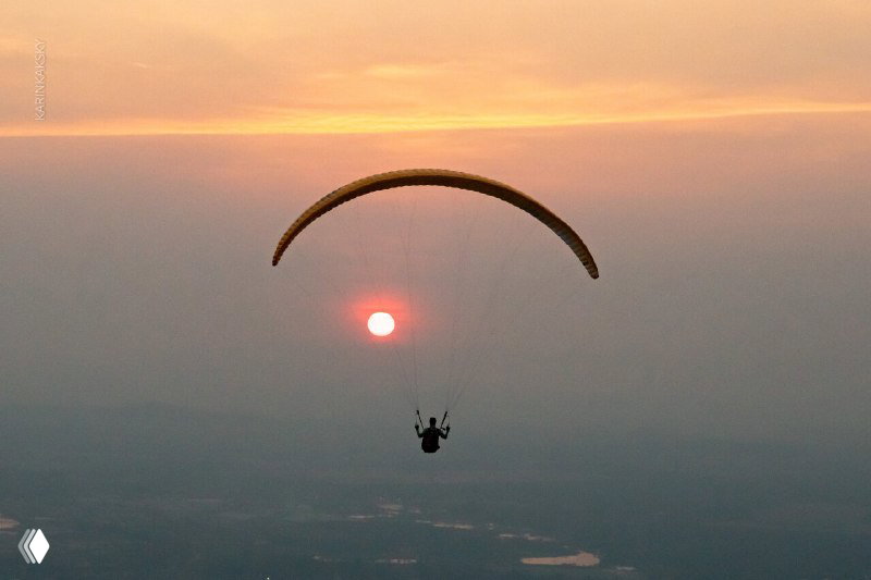 Силуэт пилота на параплане на фоне закатного солнца — атмосферный кадр, иллюстрирующий спокойный маршрутный полёт и условия видимости на высоте.