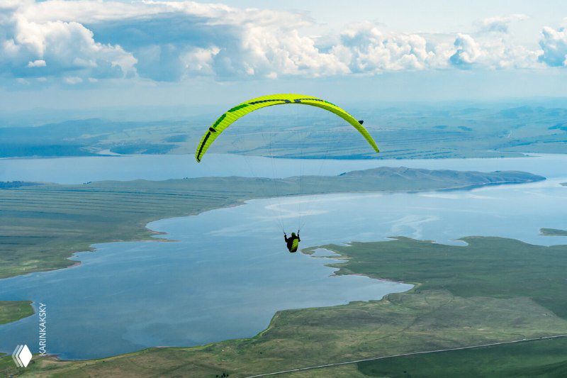 Параплан над большим водоёмом и облачным небом, пилот держит высоту и маршрут — пример использования рельефа и погодных условий для продолжительных полётов.