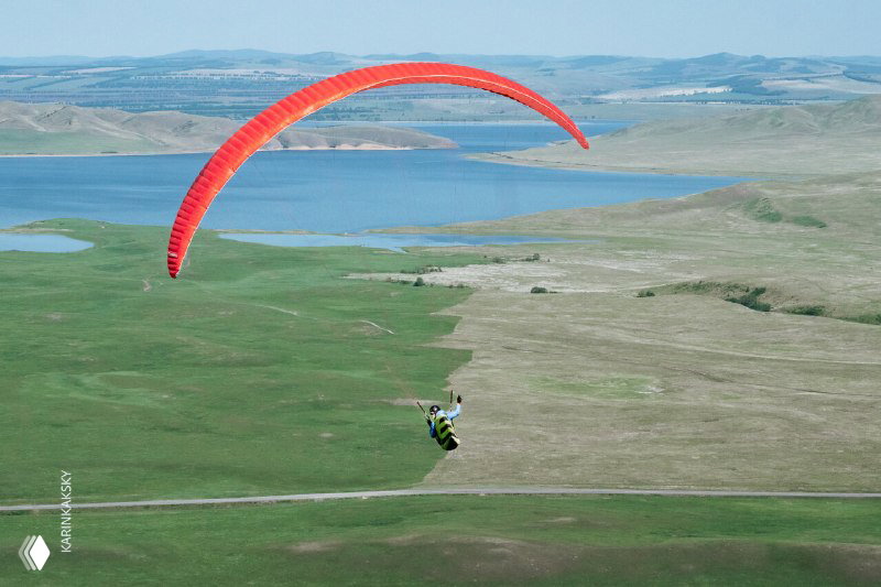 Красный параплан над степью и просёлочной дорогой, пилот выполняет маршрутный полёт над равниной — типичный вид тренировочных и маршрутных полётов.