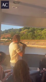 Вертикальное видео с яхты во время презентации, видно выступающего спикера и береговую линию на фоне зелёных холмов и реки.