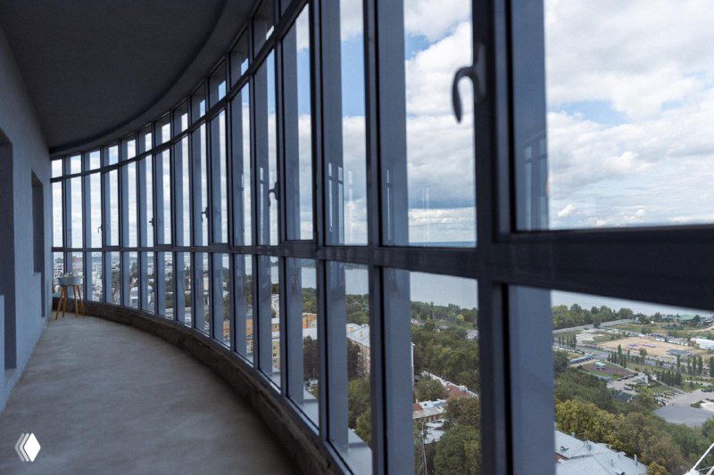 Закруглённая панорамная лоджия 24‑го этажа с панорамными окнами: вид на реку и городской пейзаж, примеры планировки остеклённой лоджии.