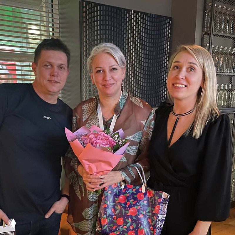 Три человека рядом, одна из женщин держит букет — кадр с визита, иллюстрирующий живое общение, обмен благодарностями и личные контакты между специалистами и командой.