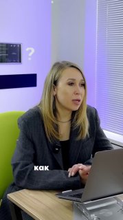 Женщина в офисной студии сидит за ноутбуком и говорит во время записи подкаста/интервью, видна цветная подсветка и надпись «как» на изображении