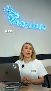 Женщина в офисе сидит за ноутбуком и говорит в камеру; на стене видна неоновая вывеска «BERLOVA.RU», деловой кадр о медицинском маркетинге.