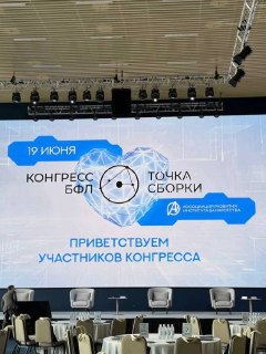 Сцена конгресса «Точка сборки»: крупный LED‑экран с датой «19 июня», логотипом мероприятия и приветственной надписью, пустые кресла в переднем плане.