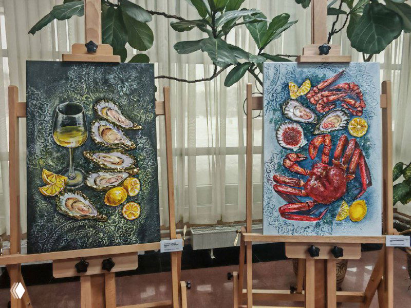 Крупный план двух картин на мольбертах: натюрморты с морепродуктами и насыщенной фактурой краски на фоне штор и растений.