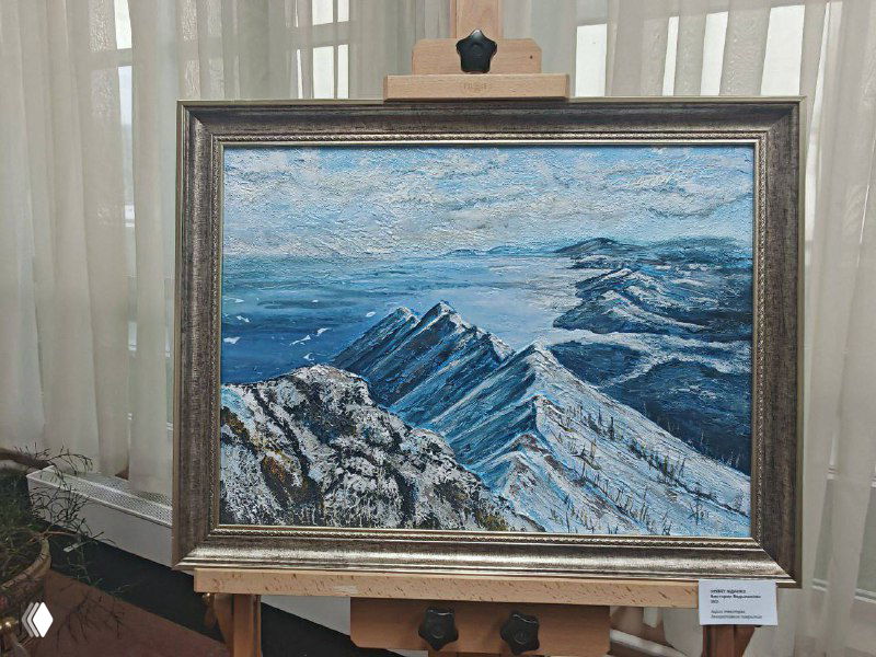 Одна из картин крупным планом: горный пейзаж с морским горизонтом, оформленная в раму и выставленная на мольберте.
