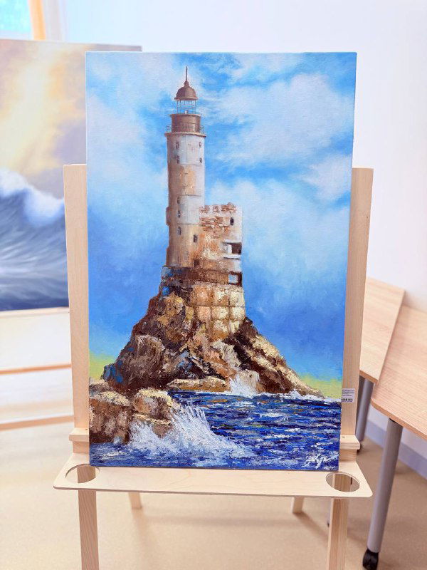 Масляная картина с маяком на скалистом мысе, пенящиеся волны и яркое голубое небо; работа выставлена на мольберте в школьной комнате.