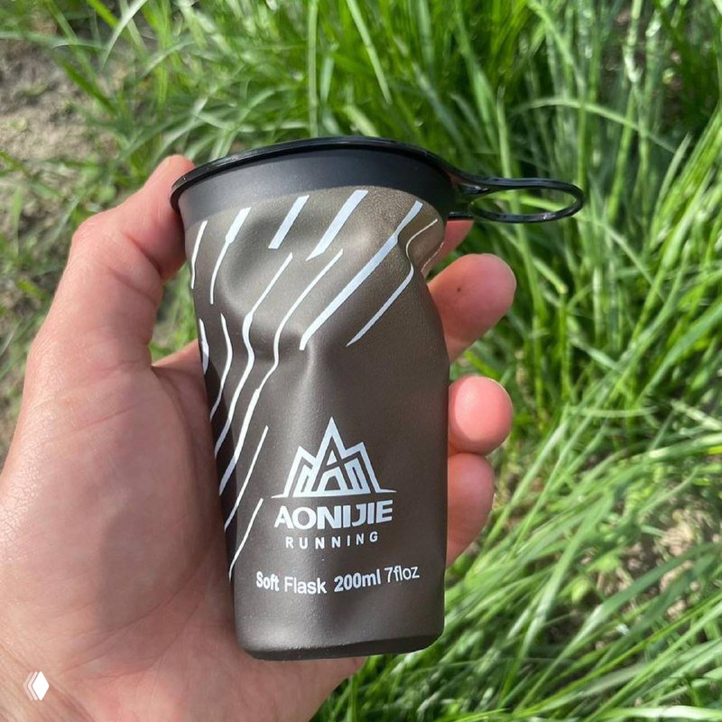 Мягкий складной многоразовый стаканчик Aonijie в руке на фоне травы; видно маркировку 200ml и конструкцию, предназначенную для отказа от пластиковых стаканов на забегах.