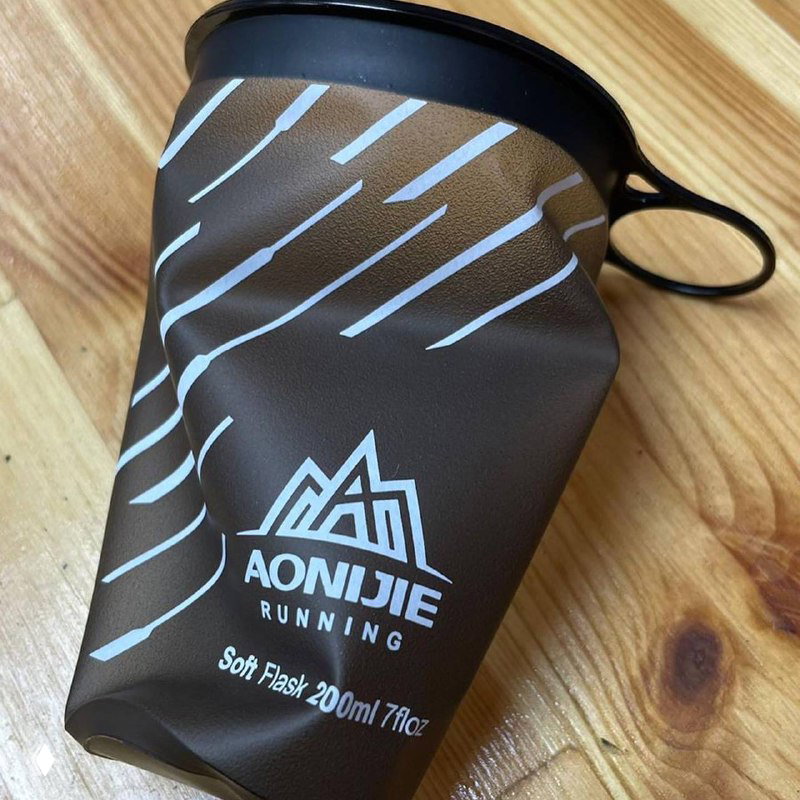 Крупный план складного многоразового стаканчика Aonijie на деревянной поверхности: виден принт бренда, форма и складной корпус, иллюстрирующие качество и компактность изделия.