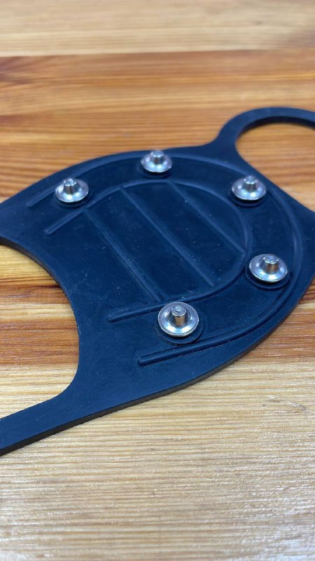 Крупный план ледоступа с металлическими шипами и заклёпками на деревянном фоне, детальная съёмка шипов и материала накладки.