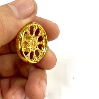 Боковой ракурс золотого миниатюрного трофея-колеса в руке, хорошо видны спицы и декоративный центр на белом фоне.