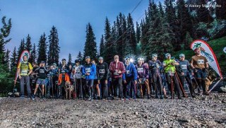 Группа участников забега на старте вечером: спортсмены в экипировке с палками и номерами, организованные в линию, видно баннеры мероприятия